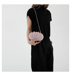 Pink glitter oval evening clutch with gold bow clasp and chain strap on a black outfit