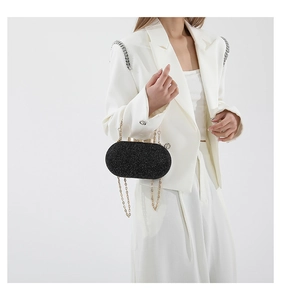 Fashionable black glitter clutch bag with gold chain strap worn by model in white suit