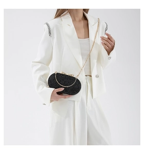 Detail of black sequin evening clutch bag featuring a gold bow clasp and chain strap