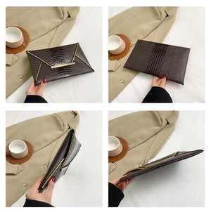 Dettagli di una borsa a busta marrone scuro con texture a coccodrillo e finiture dorate