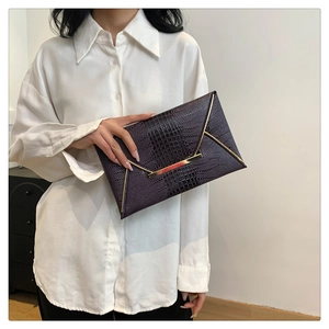 Detail of dark purple crocodile texture envelope bag with gold metal clasp on model
