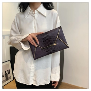 Dettaglio pochette a busta viola scuro con motivo coccodrillo e finiture dorate