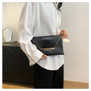 Detail of black faux crocodile skin envelope clutch bag with gold metallic trim accents