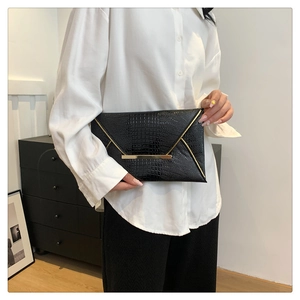 Dettaglio della pochette a busta nera con trama coccodrillo e bordo dorato tenuta dalla modella