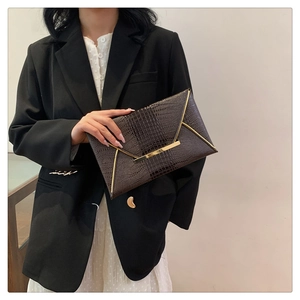 Dettaglio pochette a busta marrone scuro con stampa coccodrillo e bordo in metallo dorato
