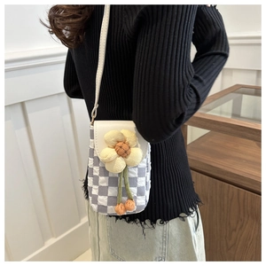 Detail of grey plaid mini crossbody bag with a decorative yellow flower charm and white strap