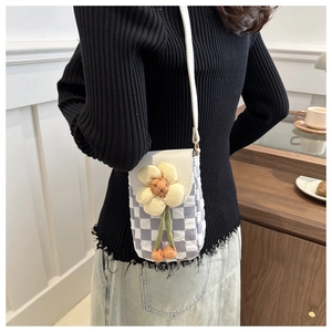 Detail view of quilted checkerboard crossbody bag with 3D floral accent on white flap