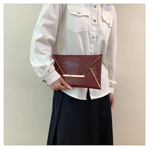 Dettaglio pochette a busta bordeaux motivo coccodrillo con finiture in metallo oro