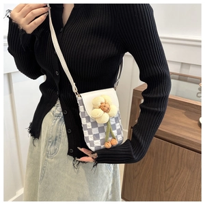 Detail of checkered crossbody phone bag with plush sunflower and white shoulder strap