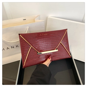 Dettaglio macro della pochette a busta bordeaux con trama coccodrillo e finiture oro