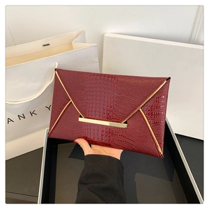 Dettaglio della pochette a busta bordeaux con finiture dorate e trama a coccodrillo