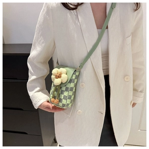 Detail view of the green checkered crossbody phone bag with a fabric flower charm