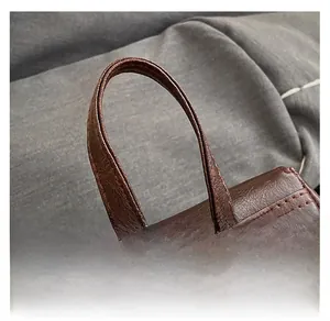 Detail of dark brown leather handle with double stitching and golden metal grommets