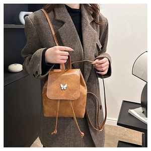 Detail of a brown leather backpack featuring a silver butterfly buckle and drawstring