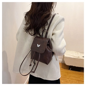 Close-up of a mini dark brown leather backpack with a decorative silver butterfly charm