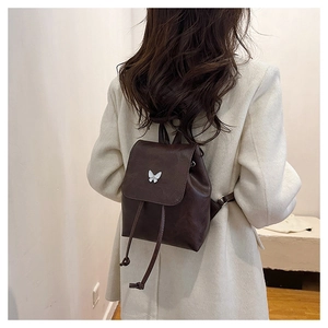 Detail of a dark brown mini leather backpack featuring a decorative white butterfly