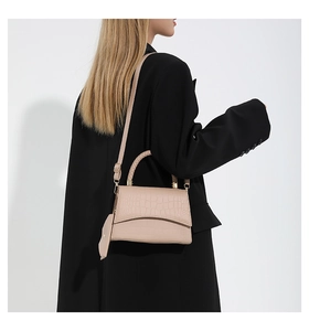 Detail of beige faux crocodile leather handbag with mini charm worn over a black blazer