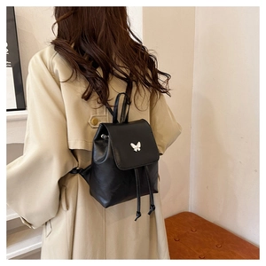 Detailed view of black PU leather backpack featuring a silver butterfly charm and drawstring