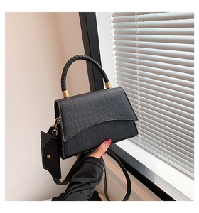 Detail of black croc-embossed handbag featuring wave-edge flap and small pouch charm