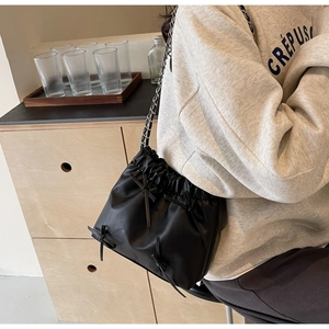 Detail of black drawstring bucket bag with bow accents and silver chain strap