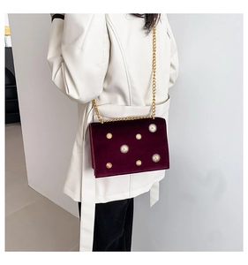 Detail of burgundy velvet shoulder bag with gold sunflower studs and chain strap