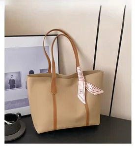 Close-up of beige tote bag featuring a pink H-logo silk scarf tied on the leather handle