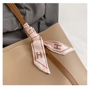 Close-up of pink silk scarf with H pattern wrapped on a beige tote bag handle