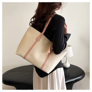 Detailed side view of a large cream tote bag with brown straps on a person's shoulder