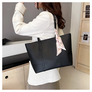 Detail of black faux leather tote bag with elegant pink ribbon and H logo on shoulder strap