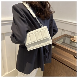 Rear view of a model wearing a white quilted flap shoulder bag with chain strap detail