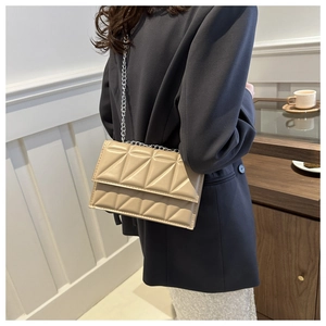 Detail of a beige quilted crossbody bag with a silver chain strap in a lifestyle setting
