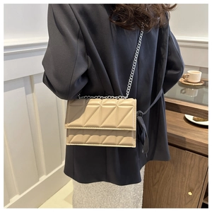 Close-up of a khaki quilted shoulder bag with silver chain strap worn over a black blazer