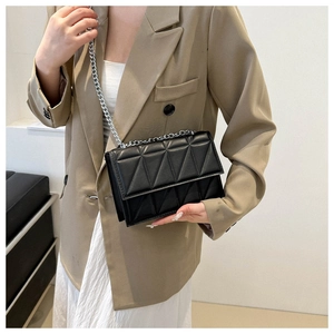 Model wearing a black quilted square bag with silver chain strap and geometric stitching