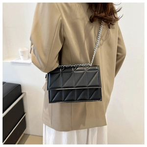 Detail of a black quilted crossbody bag with silver chain strap on a blazer model