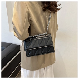 Detail of a black quilted crossbody bag with silver chain strap on a khaki blazer