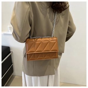 Detail view of caramel quilted crossbody bag with silver chain strap on model