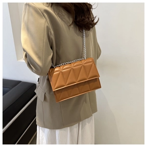 Detail of a brown quilted crossbody bag with silver chain strap on a khaki blazer