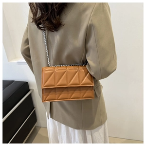 Close-up of caramel brown quilted shoulder bag with silver chain strap on model