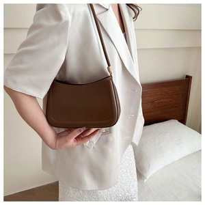 Detail of minimalist dark brown leather underarm bag with gold hardware on a model