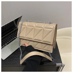 Close-up of beige quilted chain handbag with triangular stitching on a laptop background