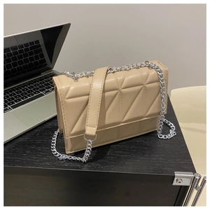 Detail of beige quilted square bag with silver chain strap on a modern dark desk
