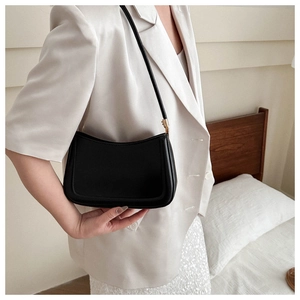 Close-up of minimalist black underarm bag with gold buckle detail on a model