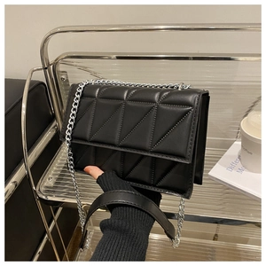 Detail of black quilted crossbody bag with silver chain on a modern metal display stand