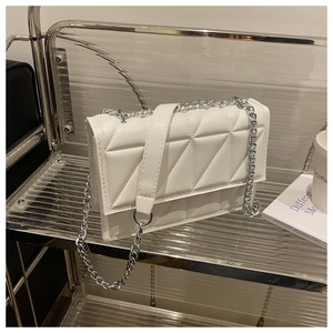 Close-up of white leather crossbody bag featuring geometric triangle quilting and silver chain