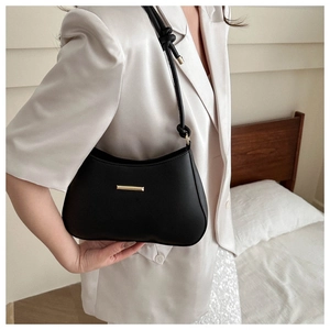 Detail of black minimalist underarm bag with gold metal trim and knotted strap detail