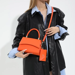 Fashionable bright orange crocodile pattern handbag with woven handle worn by model