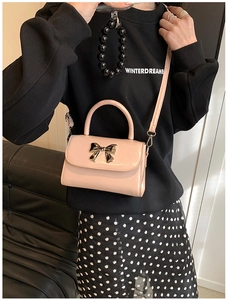 Detail of pink patent leather handbag featuring a silver metal bow buckle and small handle