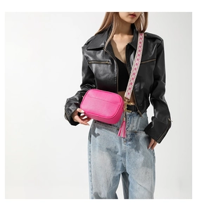 Hot pink PU leather camera bag with patterned wide strap and tassel detail on model