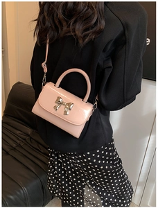 Detail of pink faux leather mini bag featuring a large silver metallic bow and top handle
