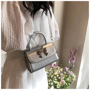 Silver mini crossbody bag with a metallic bow detail worn by a model in a white dress